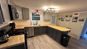Une cuisine moderne avec des meubles gris, un plan de travail en bois, une cuisinière en acier inoxydable et un luminaire suspendu rouge.