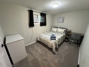 Une chambre à coucher avec un lit, un bureau, une chaise, un radiateur et une fenêtre avec des rideaux.