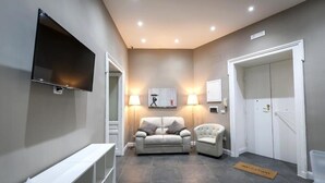 Un hall d’hôtel moderne, avec un canapé, un fauteuil et un téléviseur à écran plat fixé au mur.