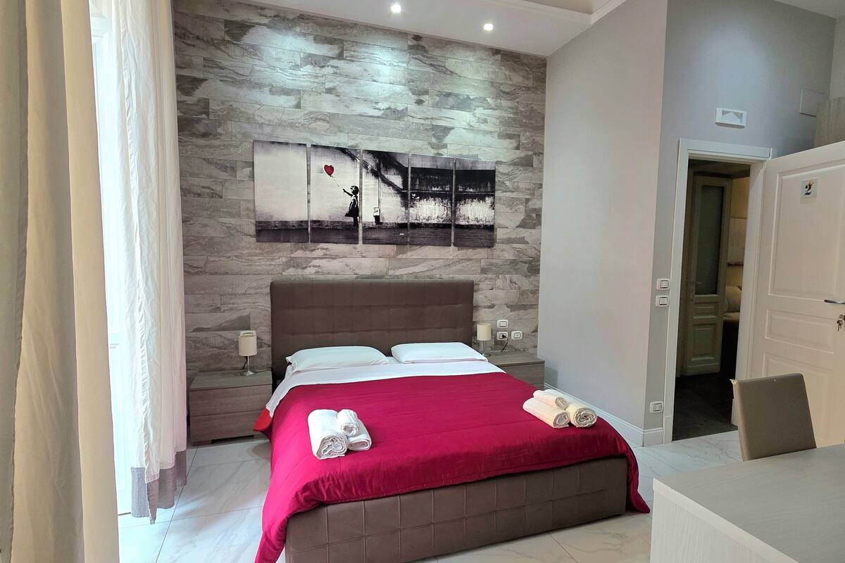 A modern bedroom with a bed, a red blanket, a marble floor, a wall art piece, and a door.