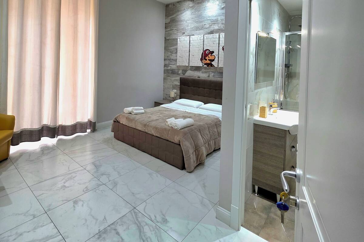 A bedroom with a bed, a bathroom with a shower, and a yellow chair.
