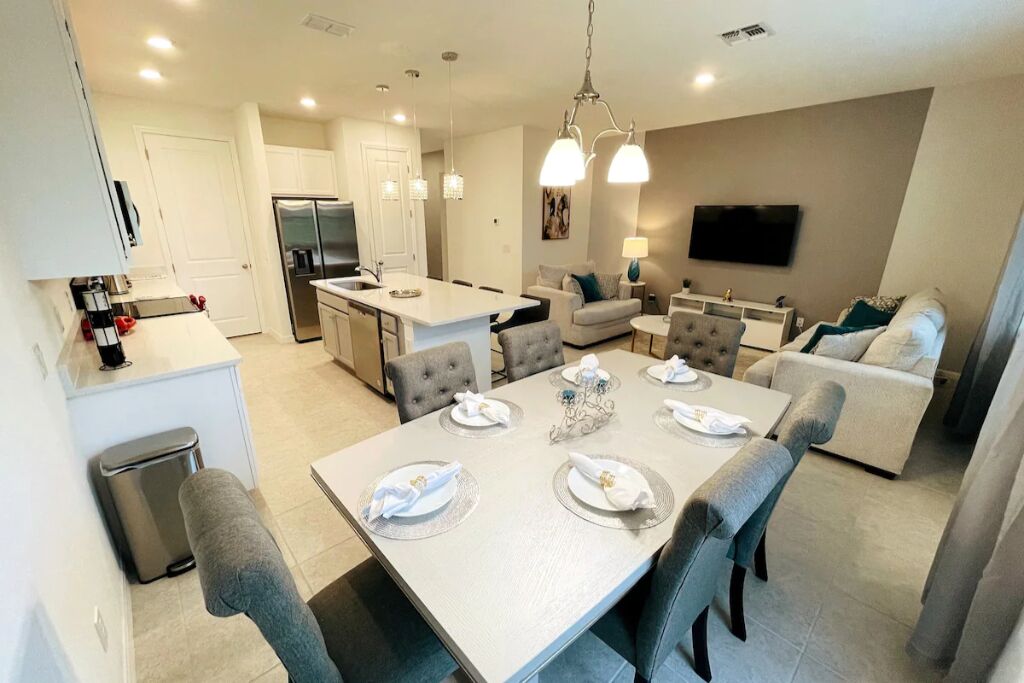 A modern kitchen with white cabinets, a stainless steel refrigerator, and a dining area with a table set for four.