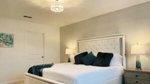 A bedroom with a white bed, dark green pillows, a white headboard, a nightstand with a lamp, and a door. - Your house 20 minutes from Disney, with pool area (Davenport)