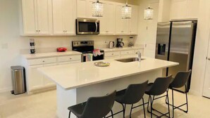 A modern kitchen with white cabinetry, a central island with bar stools, stainless steel appliances, and pendant lighting. - Your house 20 minutes from Disney, with pool area (Davenport)