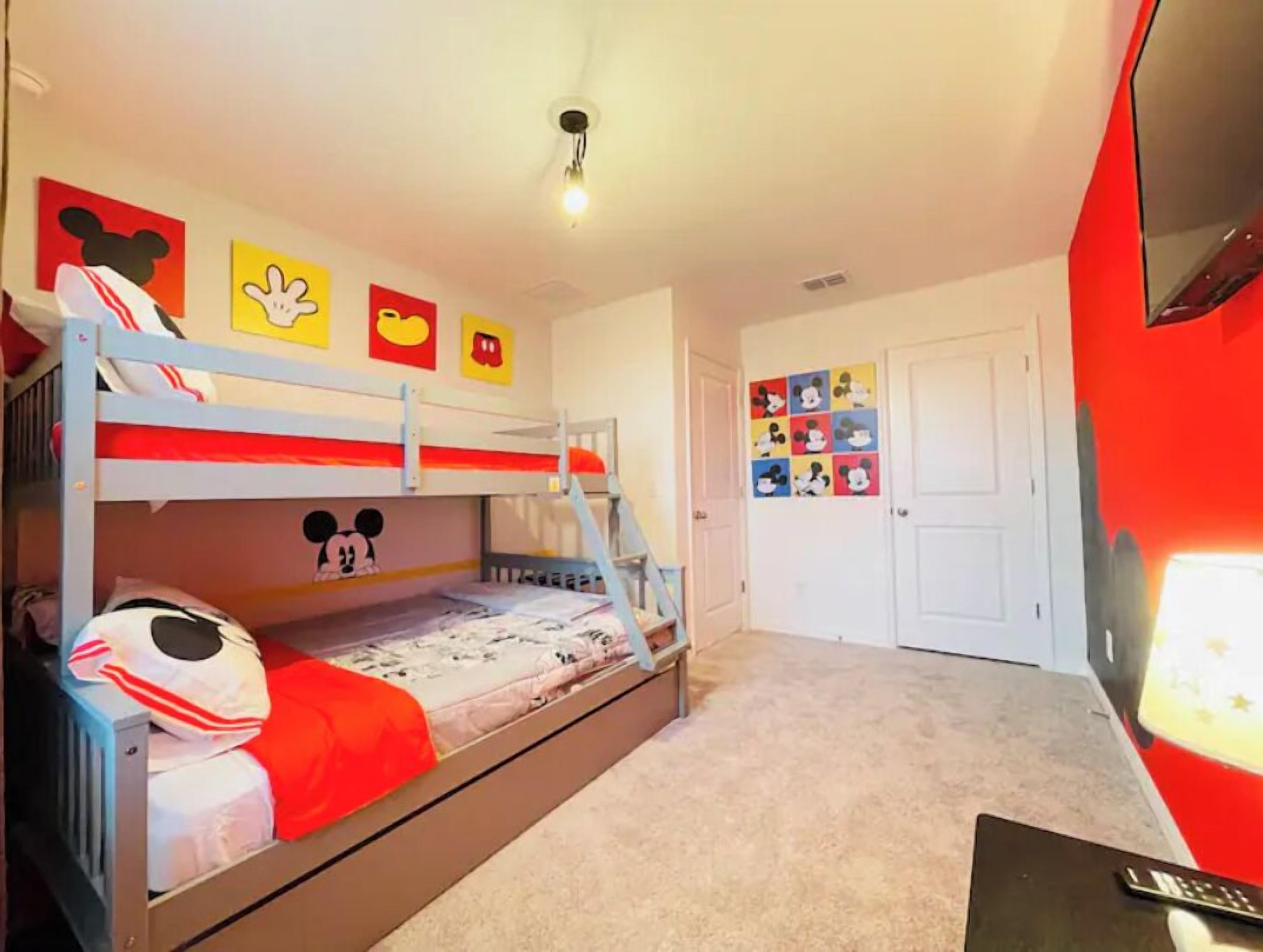 Un lit superposé décoré aux motifs de Mickey Mouse, une porte blanche et un mur rouge.