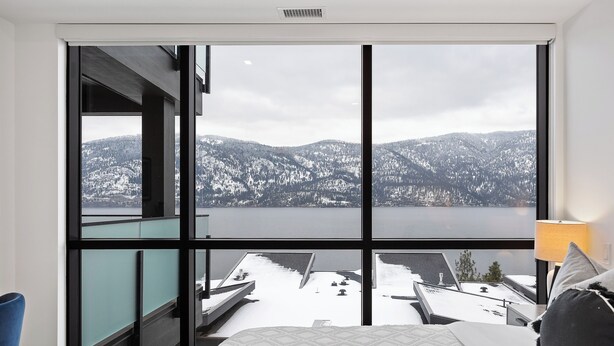 Ein Schlafzimmer mit großem Fenster mit Blick auf eine verschneite Landschaft und ein Gewässer.