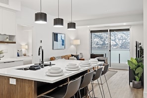A modern kitchen with a central island, pendant lighting, and a view of a snowy landscape through large windows.