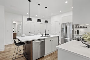 A modern kitchen with white cabinetry, stainless steel appliances, and black pendant lighting.