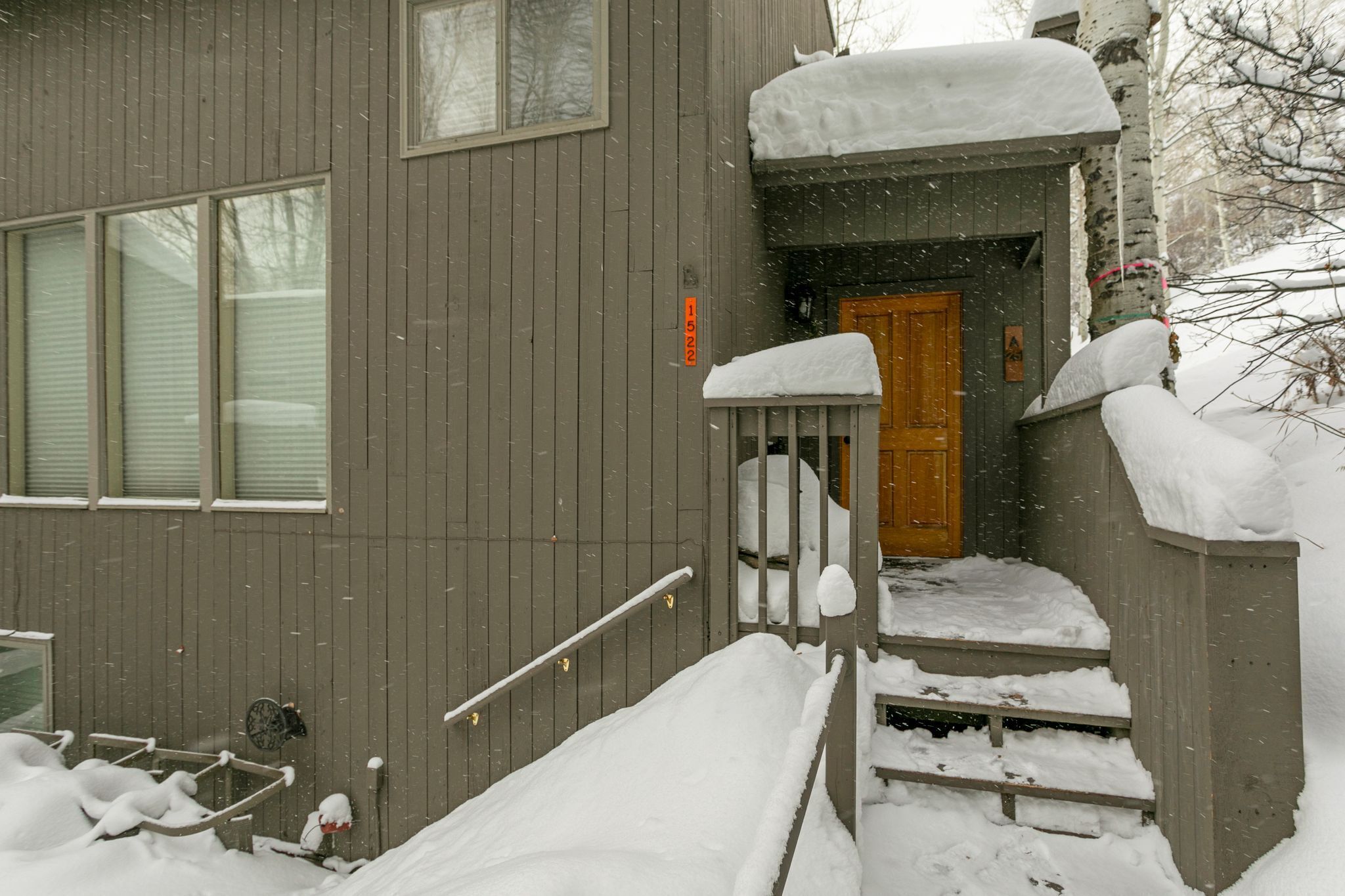 A wooden house with a wooden door and steps leading to the entrance. Snow is piled on the steps and around the house.