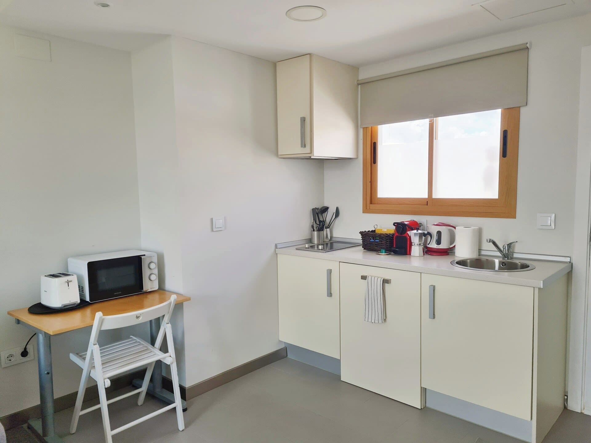 A compact kitchen with a microwave, toaster, and a small dining table with a chair.