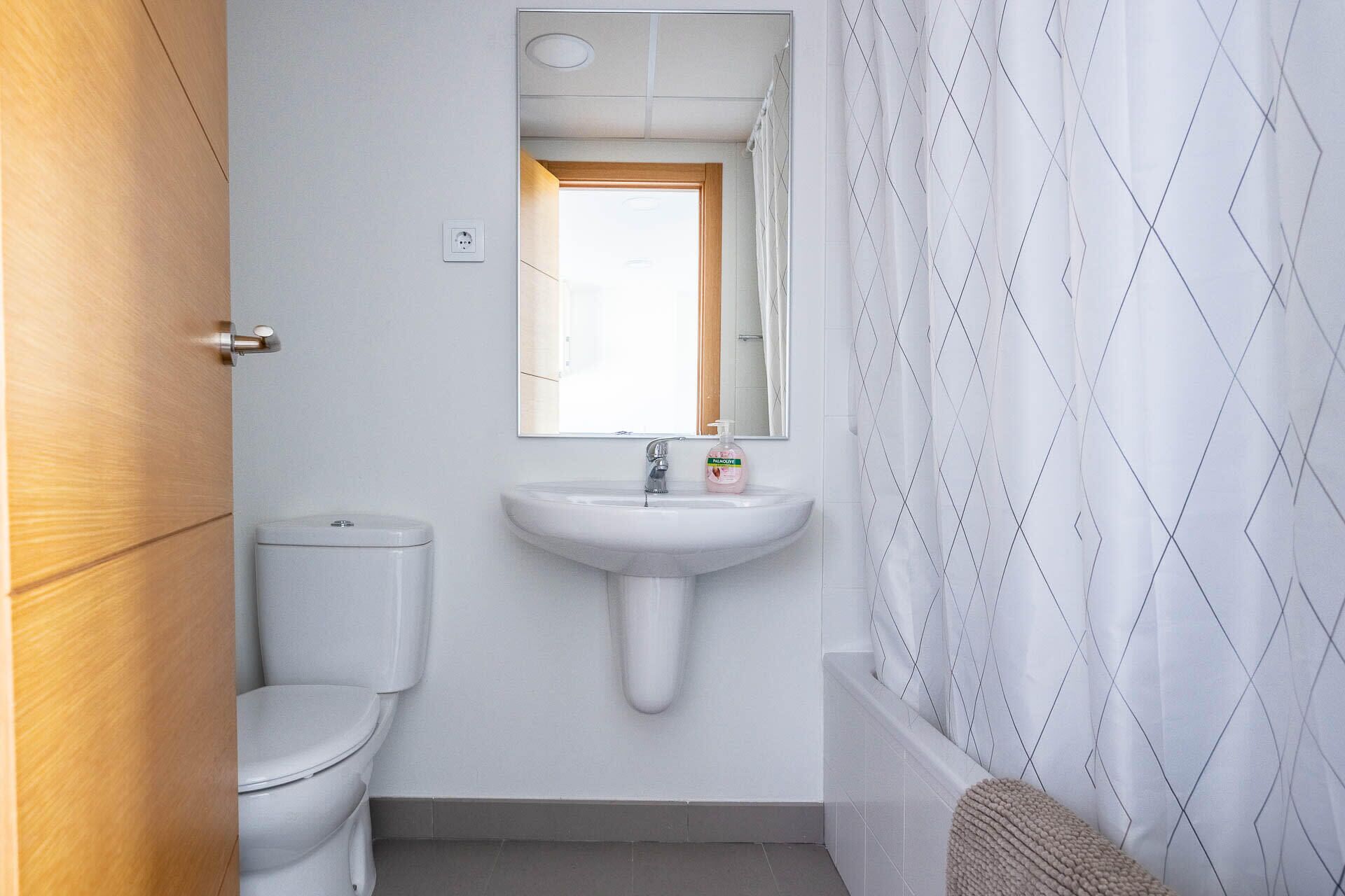 A small, clean bathroom with a toilet, sink, and mirror.