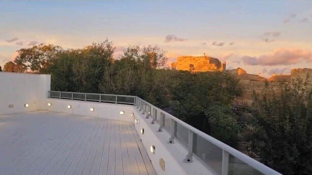 A rooftop terrace with a railing, trees, and a distant view of a historic building.