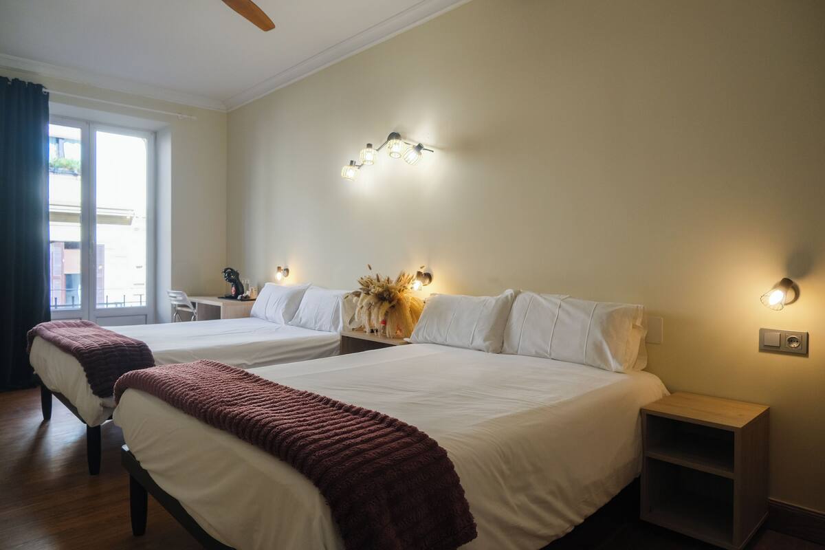 A hotel room with two beds, a desk, and a chair. There are wall sconces providing light.