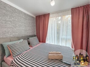 Relax in comfort with a large bed, striped bedspread, and sheer curtains framing a scenic outdoor view.