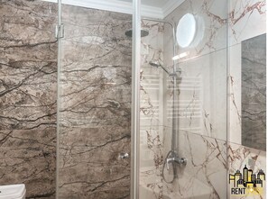 Bathroom features a glass-enclosed shower area, handheld showerhead, and a round mirror.
