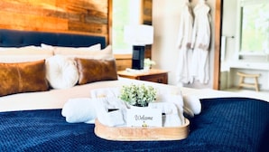 Habitación de hotel con cama, pared de madera, ventana y bandeja con toallas y un cartel de bienvenida.