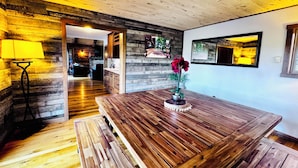 Una mesa de comedor de madera con un jarrón de flores, una lámpara y vistas hacia una zona de cocina.