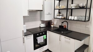 A modern kitchen with white cabinets, a black countertop, a built-in oven, a sink, and a shelf with kitchenware.