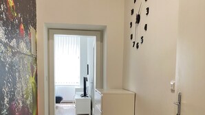 A hallway with a geometric patterned floor, a small white side table, a wall clock, and a door leading to another room.