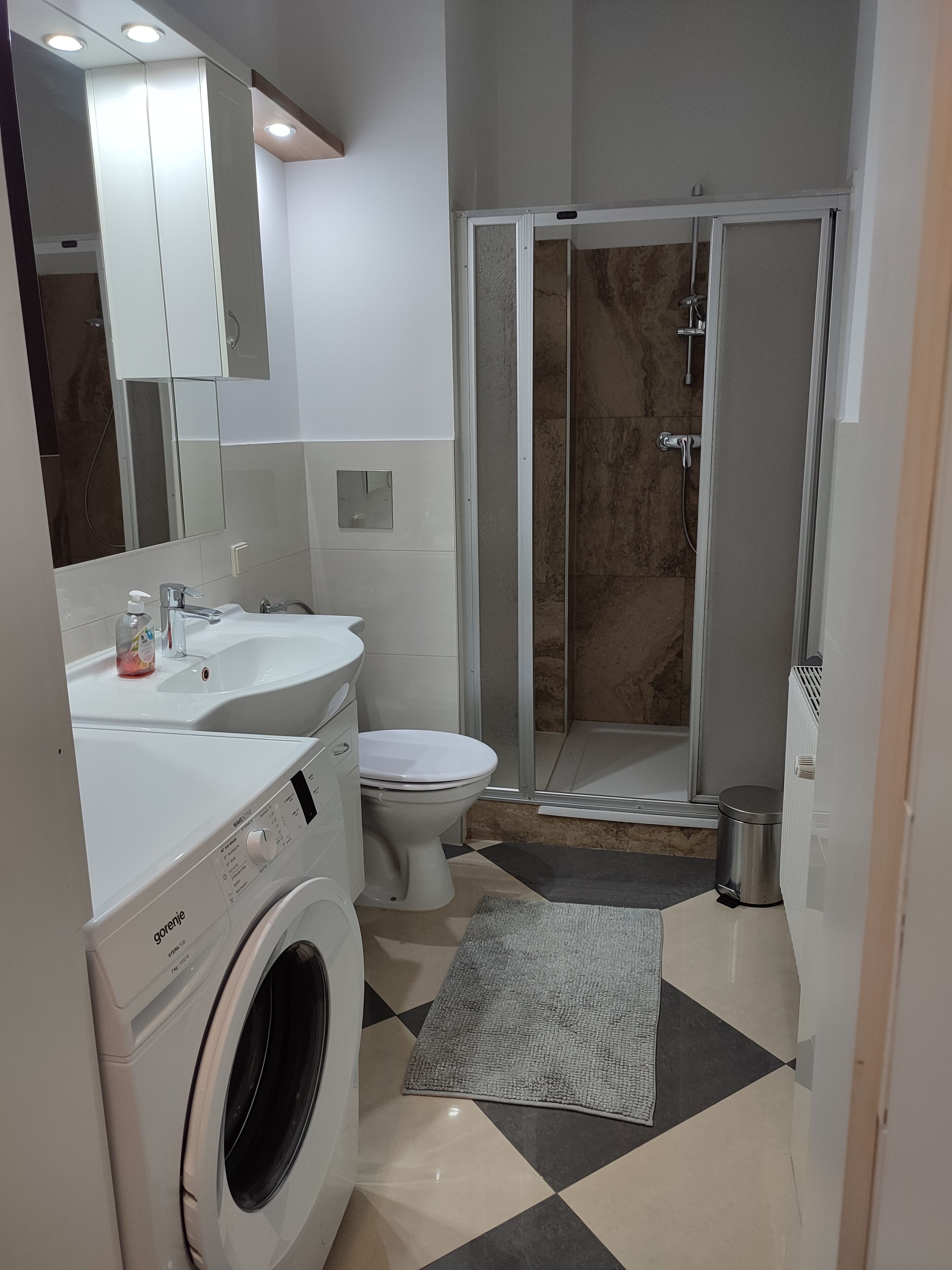 A modern bathroom with a washing machine, toilet, and shower area.