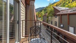 Ein Balkon mit Metallgeländer, einem Holztisch und Blick auf eine Berglandschaft im Herbstlaub.
