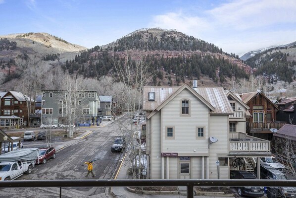 A town with a mix of residential and commercial buildings, a street with parked cars, and a hilly backdrop.