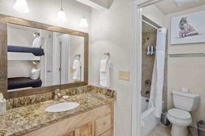Une salle de bain avec un lavabo sur un plan de travail en granit, un meuble-lavabo en bois, un grand miroir, une douche avec une porte en verre et des toilettes.