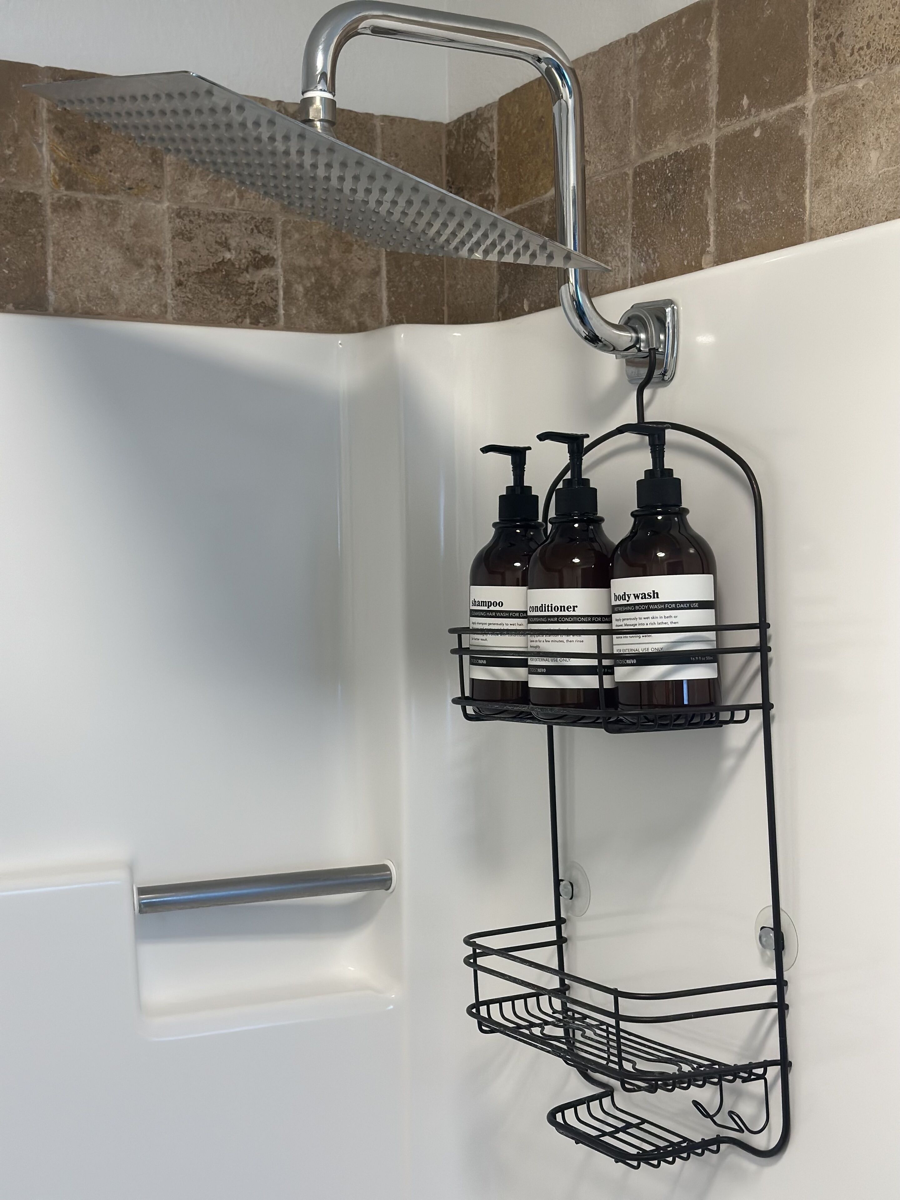 Une salle de bain avec une douche, une baignoire blanche, un porte-serviettes et deux étagères où sont rangées des bouteilles de gel douche et d’après-shampoing.