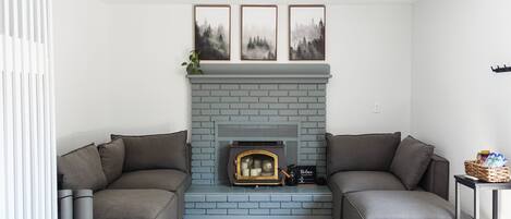 A living room with a gray brick fireplace, gray sofas, a patterned rug, and three framed pictures above the fireplace.