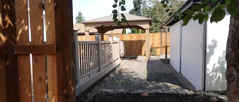 A fenced backyard with a covered patio area, a shed, and a tree.