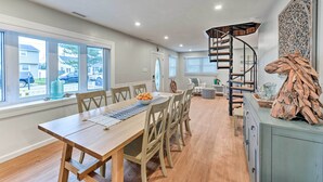 Un comedor con mesa de madera, sillas y vistas al exterior. Se observa una escalera de caracol que lleva a otro nivel.