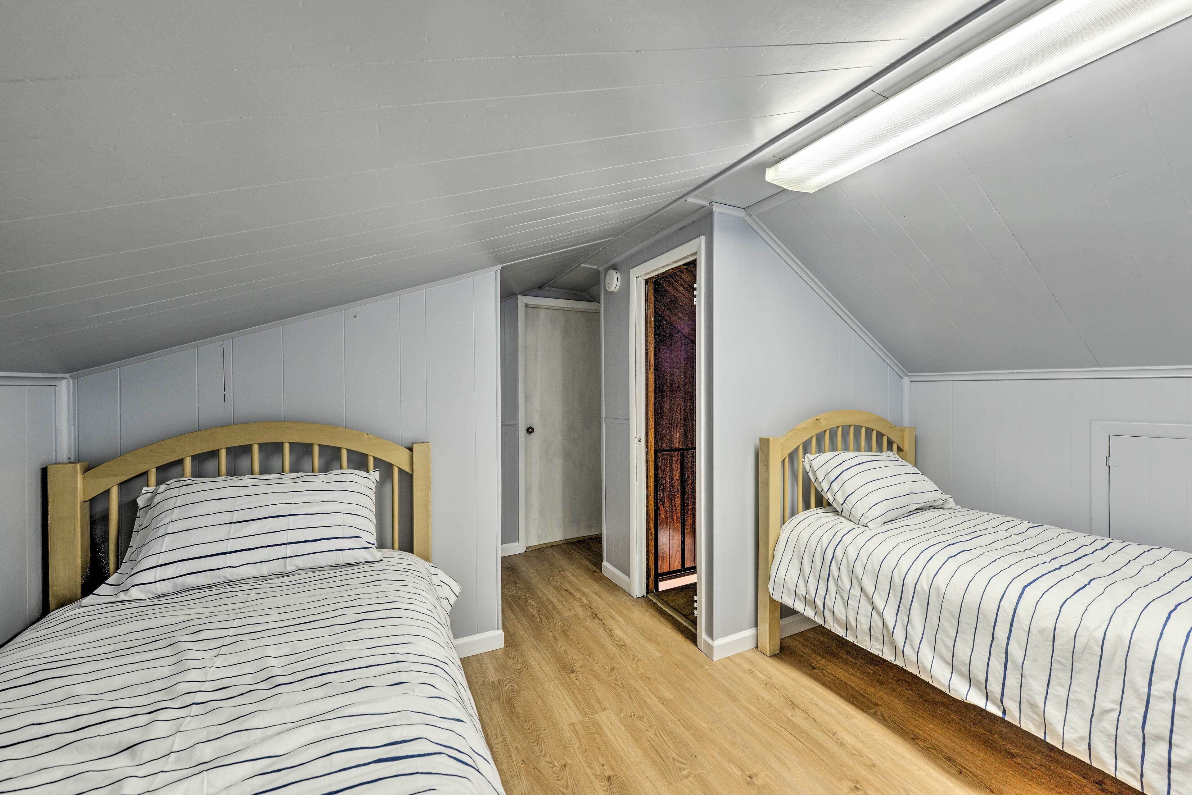 Une chambre avec deux lits simples, des têtes de lit en bois et un plafond en pente agrémenté d’un luminaire.