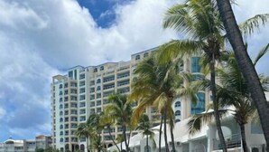 A coastal hotel with a stone retaining wall, a paved walkway, and palm trees. - Oceanfront, 4 balcony condo: Stunning Sunsets (Sint Maarten)