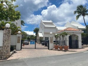 A gated entrance with a white building, stone pillars, and a paved walkway. - Oceanfront, 4 balcony condo: Stunning Sunsets (Sint Maarten)