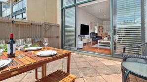 An outdoor patio with a wooden table set for dining, a wine bottle, and wine glasses.