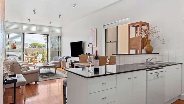 A modern kitchen with white cabinetry, a black countertop, and a built-in dishwasher.