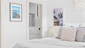 A bedroom with a bed, a nightstand, a mirror, and a door leading to a bathroom.