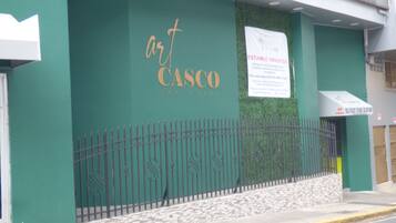 L’entrée d’un hôtel, avec une façade verte, une clôture en métal et une enseigne indiquant « CASCO THE HOTEL ».