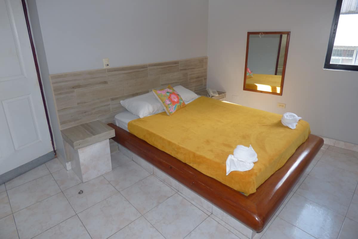 A hotel room with a bed, bedside table, a mirror, and a window.