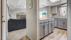 Une cuisine moderne avec des meubles gris, une cheminée en briques et une vue sur le jardin arrière.