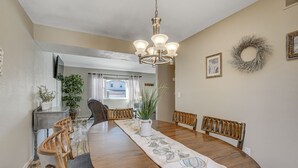 Une salle à manger avec une table en bois, des chaises, un lustre et un long chemin de table.