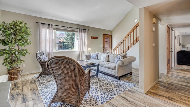 Un salon comprenant un canapé, deux fauteuils en osier, une table basse, une plante en pot et un tapis à motifs.