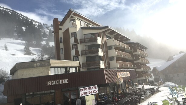 A multi-story building with balconies, a sign for 'LA BUCHERIE', and a 'BRASSERIE BAR-SNACK' sign. - Charming snow front studio (Auris)