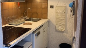 A compact kitchen with white cabinets, a microwave, a sink, and a dish rack. - Charming snow front studio (Auris)