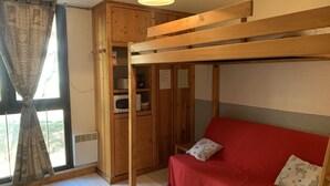 A room with a bunk bed, a red sofa, a wooden cabinet, and a window with curtains. - Charming snow front studio (Auris)
