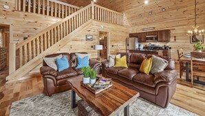 A spacious living area with a wooden staircase, leather sofas, and a kitchen in the background. - Family Friendly Cabin, Mountain Views, Easy Roads, Pool, Hot Tub, Game Room (Gatlinburg)