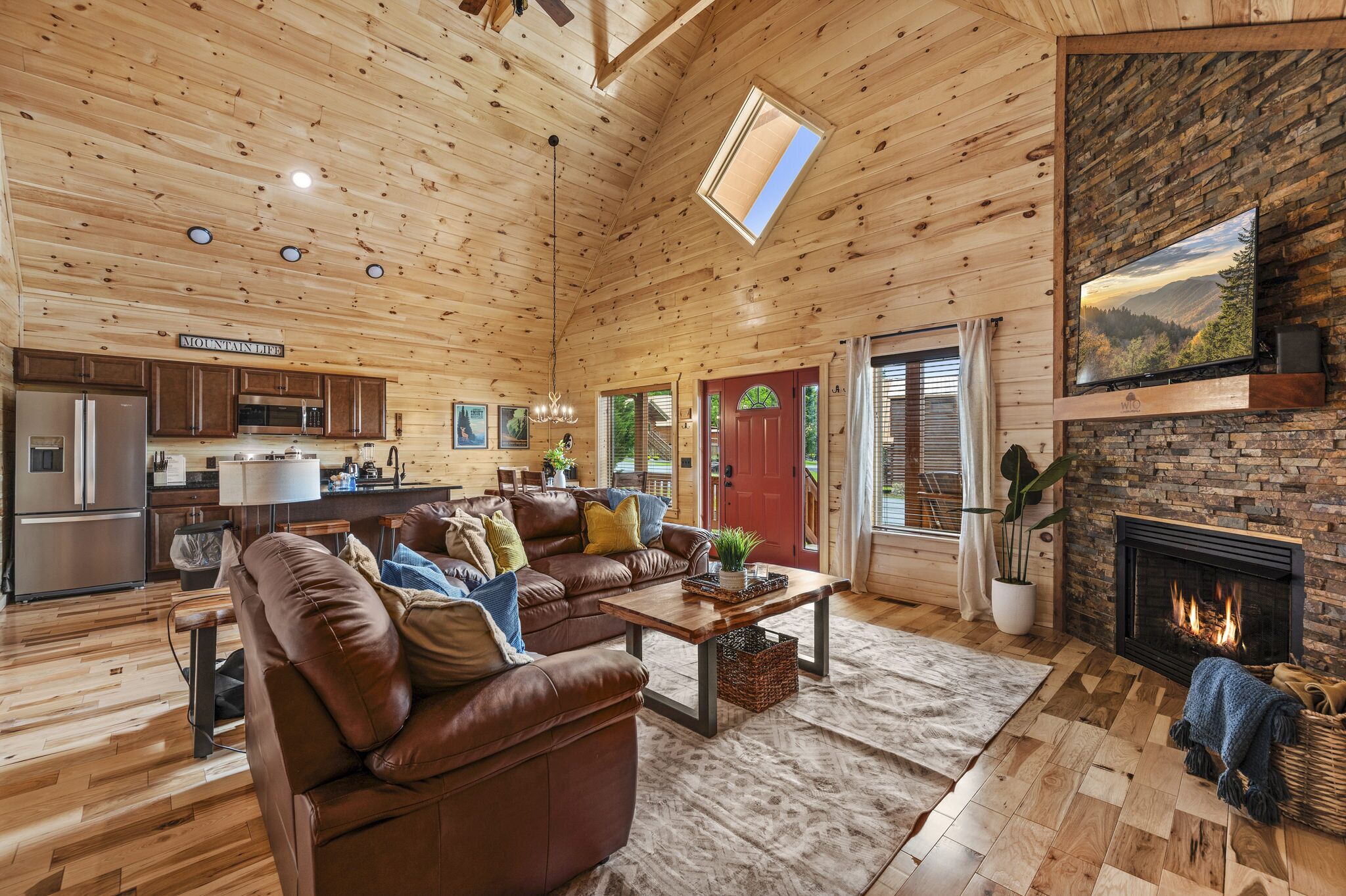 A spacious living room with a fireplace, a cozy fireplace area, and a kitchen with wooden cabinets and a stainless steel refrigerator.
