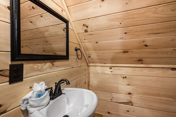 A wooden-paneled bathroom with a white sink, black faucet, and a mirror.