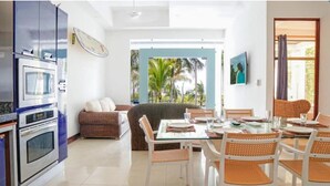A modern kitchen with built-in appliances, a dining area with a glass table and wicker chairs, and a view of palm trees through a large window. - Oceanfront Pool Paradise Villa (Provincia de Puntarenas)