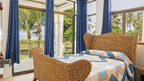 A room with a wicker bed, a view of palm trees, and a balcony with blue curtains. - Oceanfront Pool Paradise Villa (Provincia de Puntarenas)